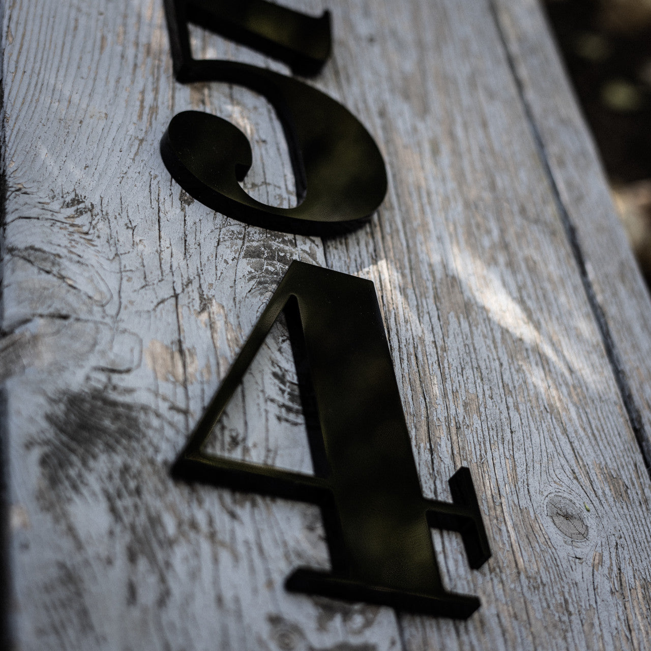 Black house numbers '54' made of metal, attached to a wooden surface, with a focus on the number '4'.