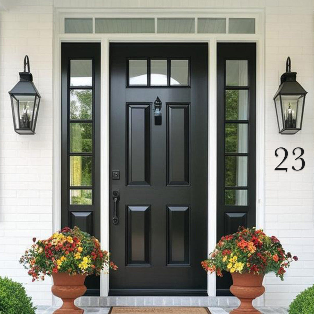 Black front door with glass panels flanked by two lamps and flower pots on a white wall. Black house numbers in a traditional cottage style.