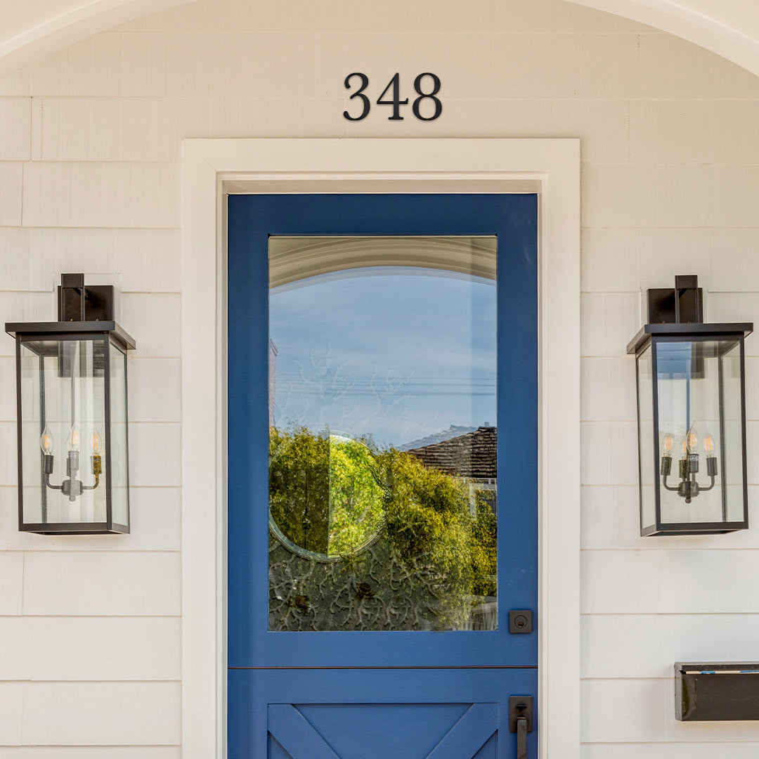 Blue front door with glass panel and 4 inch traditional style black metal house number '348' on a white wall.