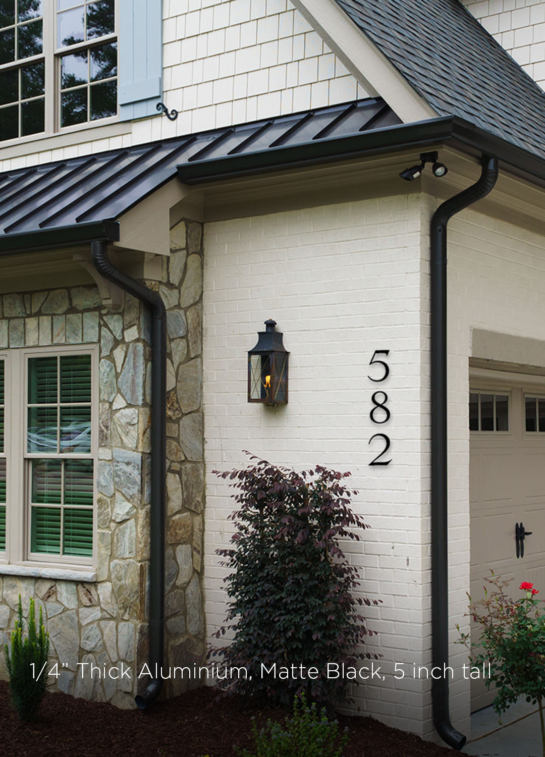 House exterior with stone and brick walls, black metal roof, and house numbers '582'. House numbers in black metal 5 inch tall