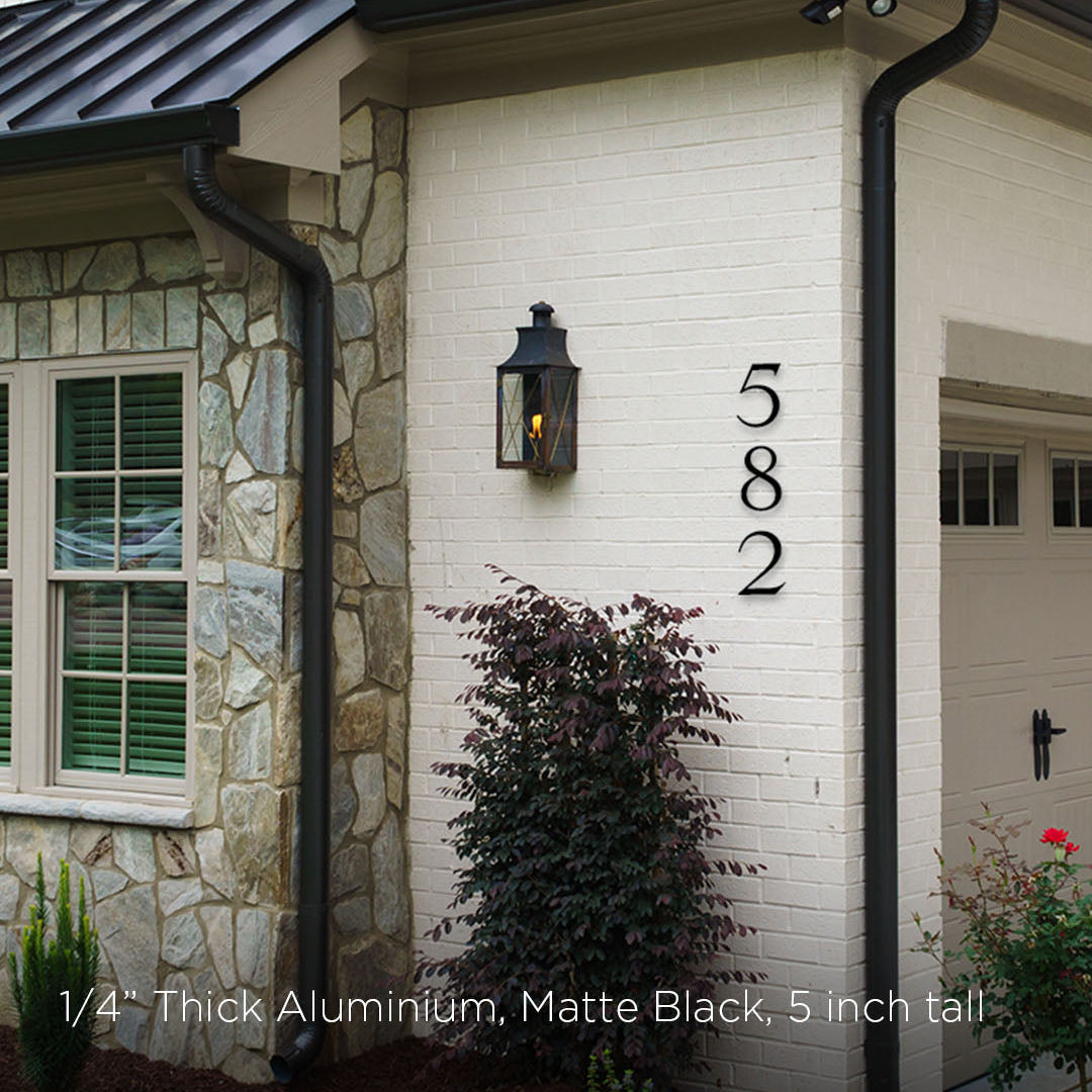 House exterior with stone and brick walls, black metal roof, and house numbers '582'. House numbers in black metal 5 inch tall