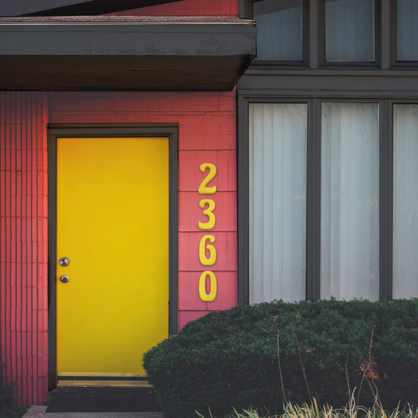 Modern house with a red exterior and yellow door yellow custom house numbers '2360' in a 1970's style house numbers