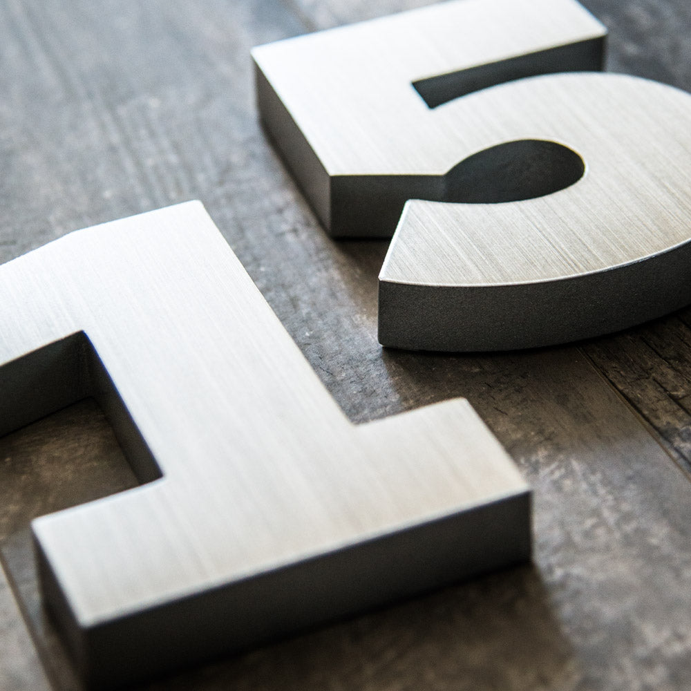 A close-up of metallic house numbers '15' placed on a wooden surface.