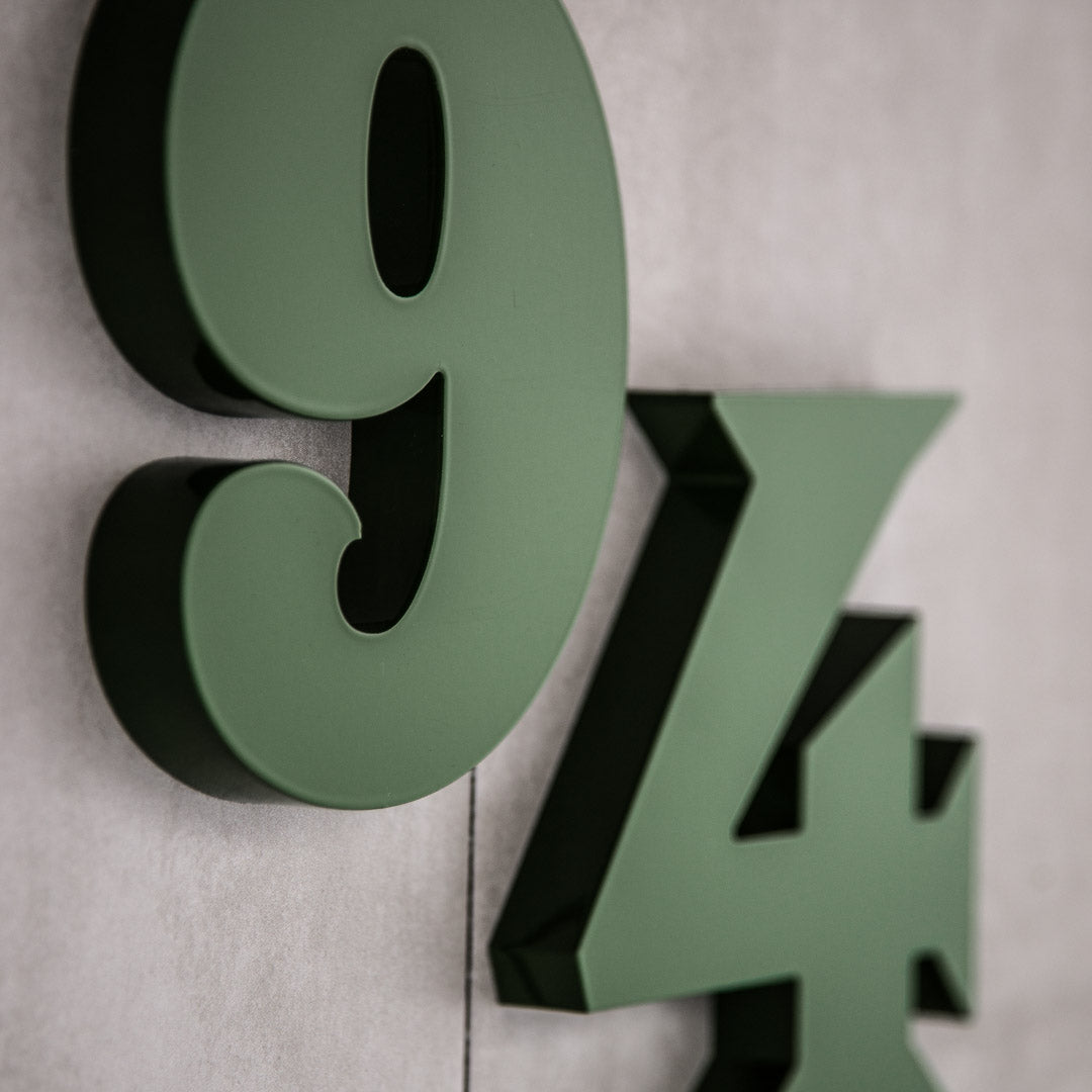A close-up of green house numbers '94' mounted on a gray background.