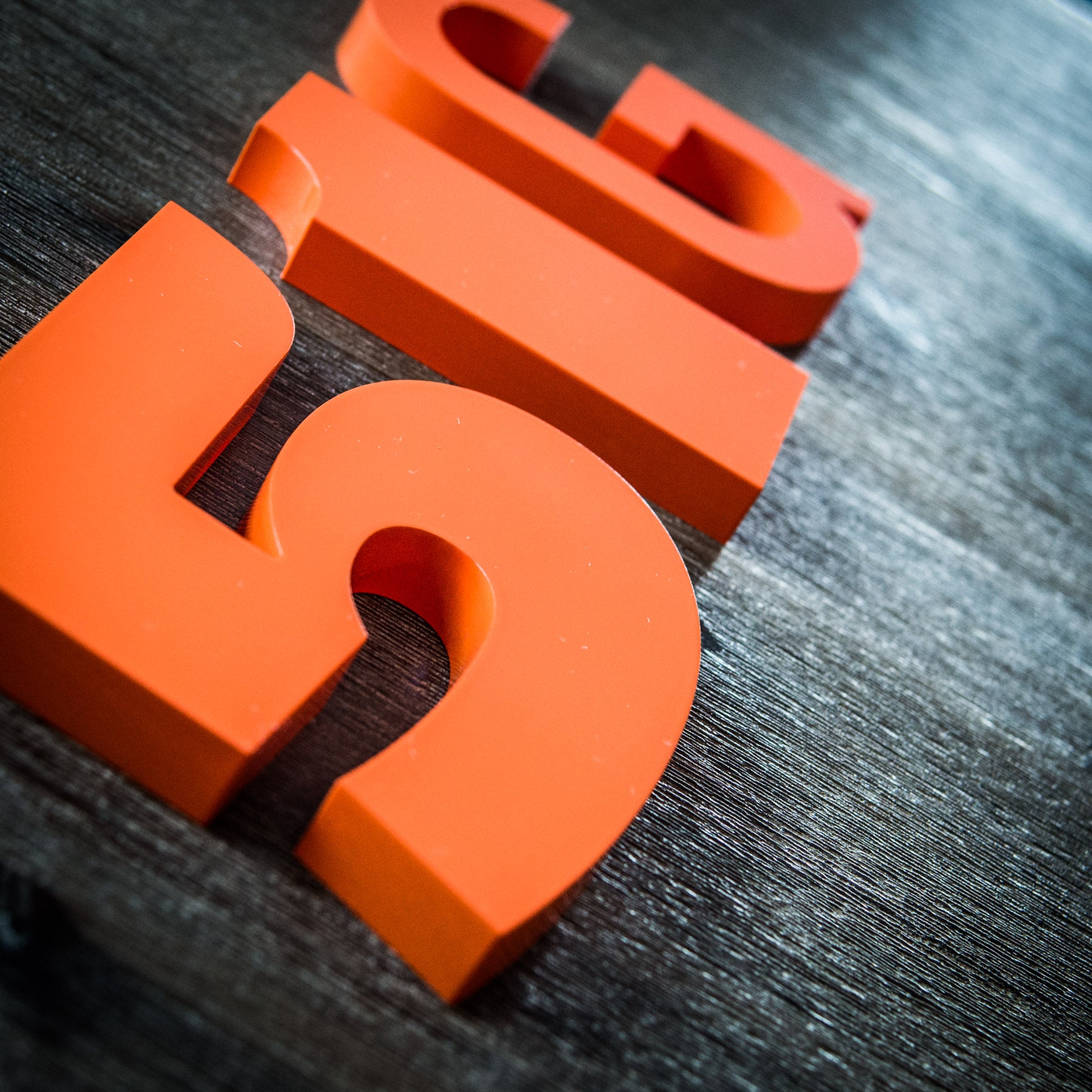 A close-up image of orange 3D printed house numbers placed on a wooden surface.