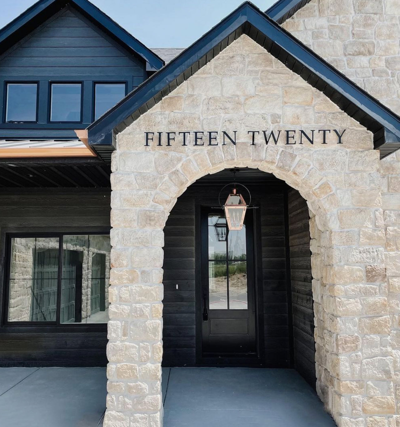 Traditional style house numbers 'FIFTEEN TWENTY' mounted on a stone archway leading to a house entrance.