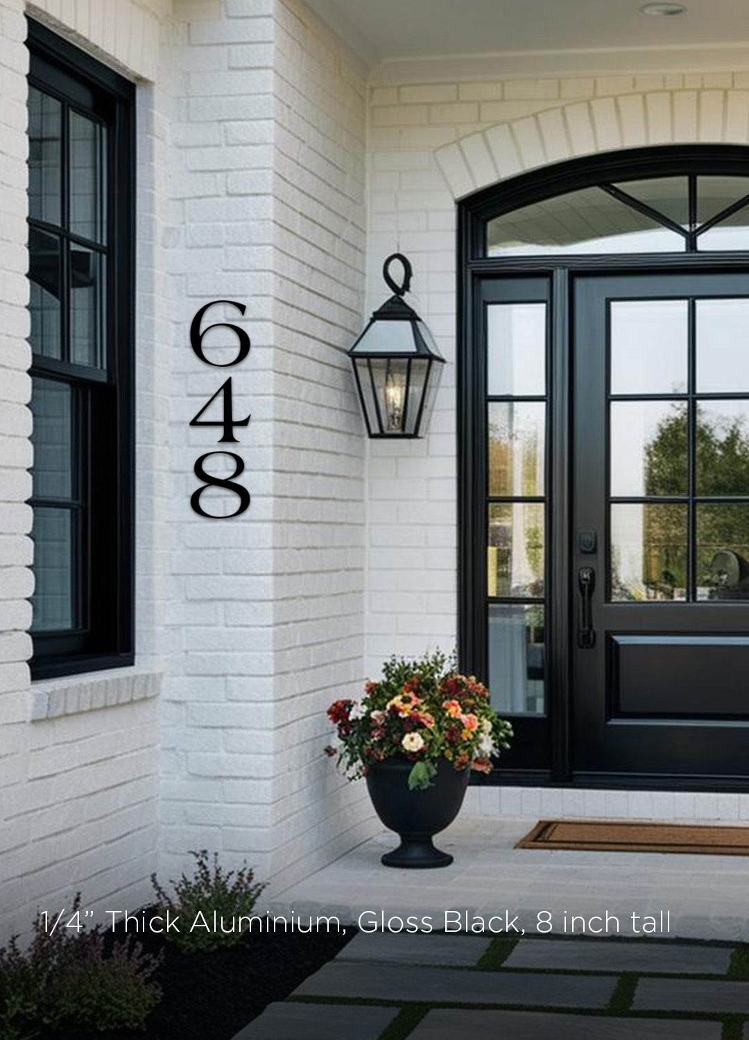 House exterior with farmhouse style address numbers '648' on a white brick wall, black door, and flower pot.