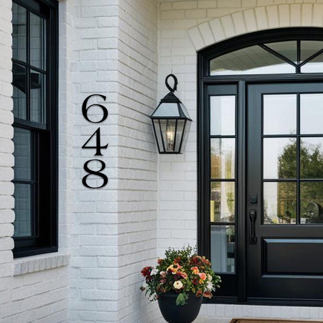 House exterior with farmhouse style address numbers '648' on a white brick wall, black door, and flower pot.