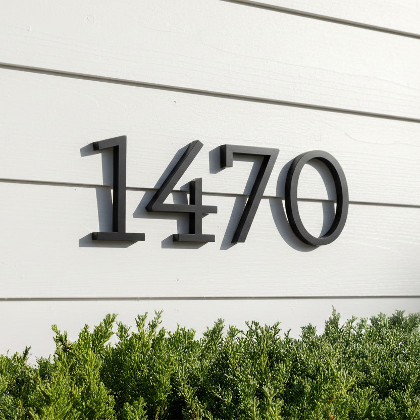 Modern house numbers '1470' on a white wall with greenery at the bottom.