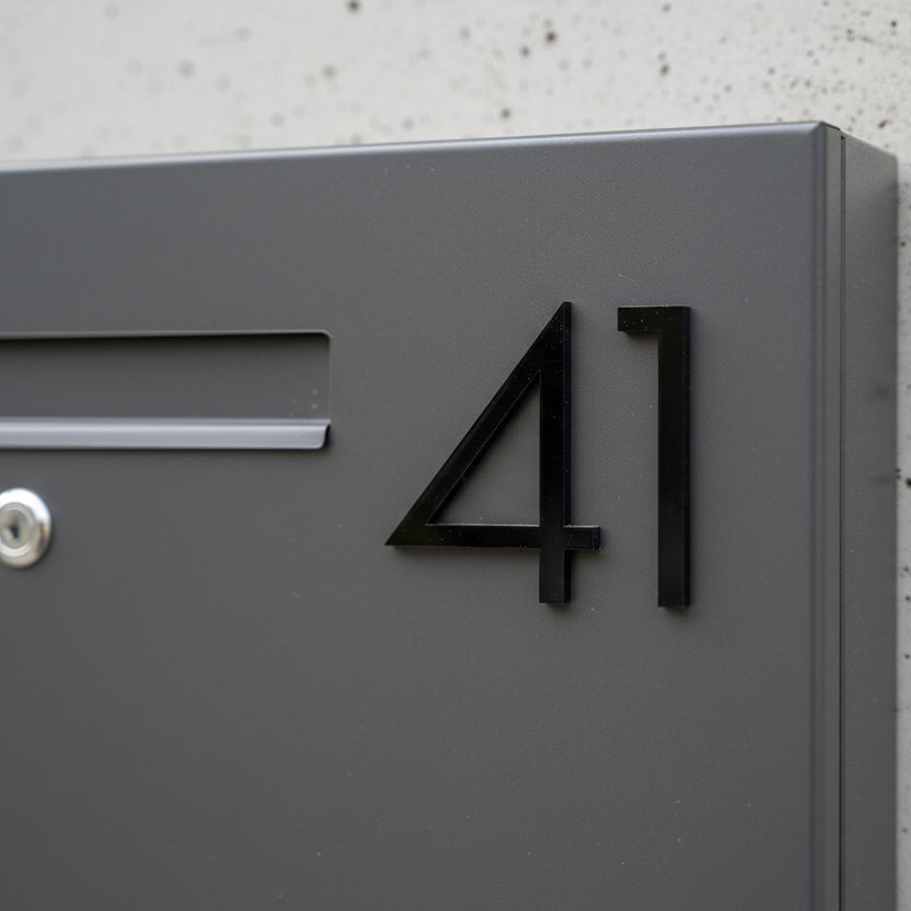 Modern house number '41' on a gray mailbox against a concrete wall.