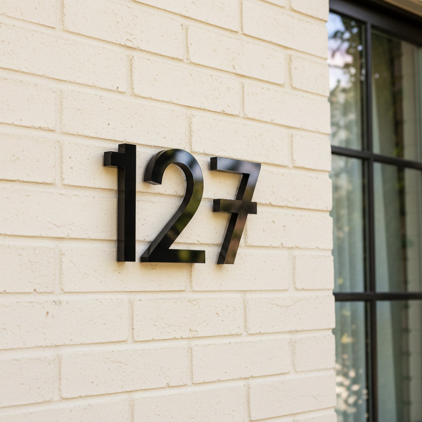 Modern house numbers '127' on a light brick wall.