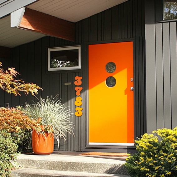 A house with orange house numbers and letters attached to the front door, set against a dark background wall. House numbers in a 1970's style