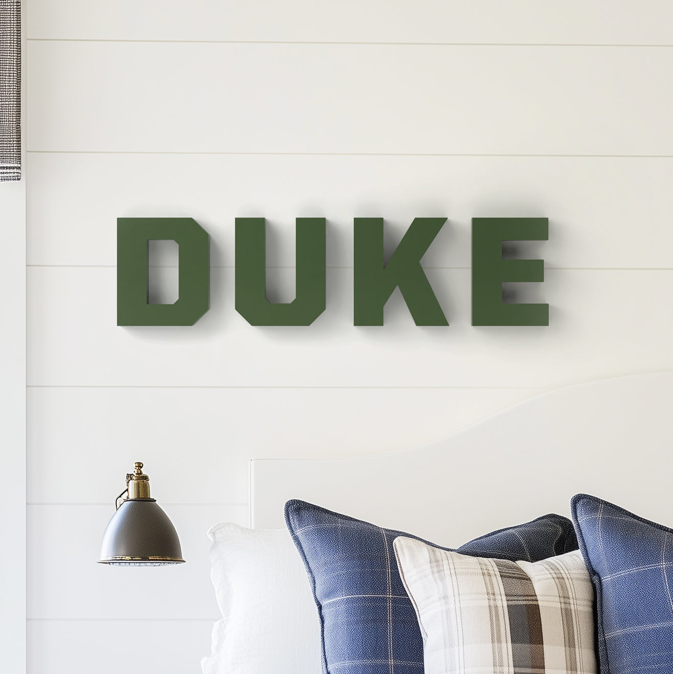 Customizable wall decor letters spelling 'DUKE' mounted on a white wall above a cushioned chair, with a lamp and decorative pillows in the setup.