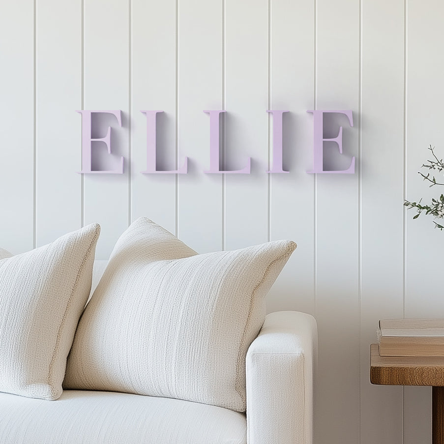 Customizable wall decor letters spelling out the name 'ELLIE' mounted on a white wall above a beige sofa, with a minimalist design.