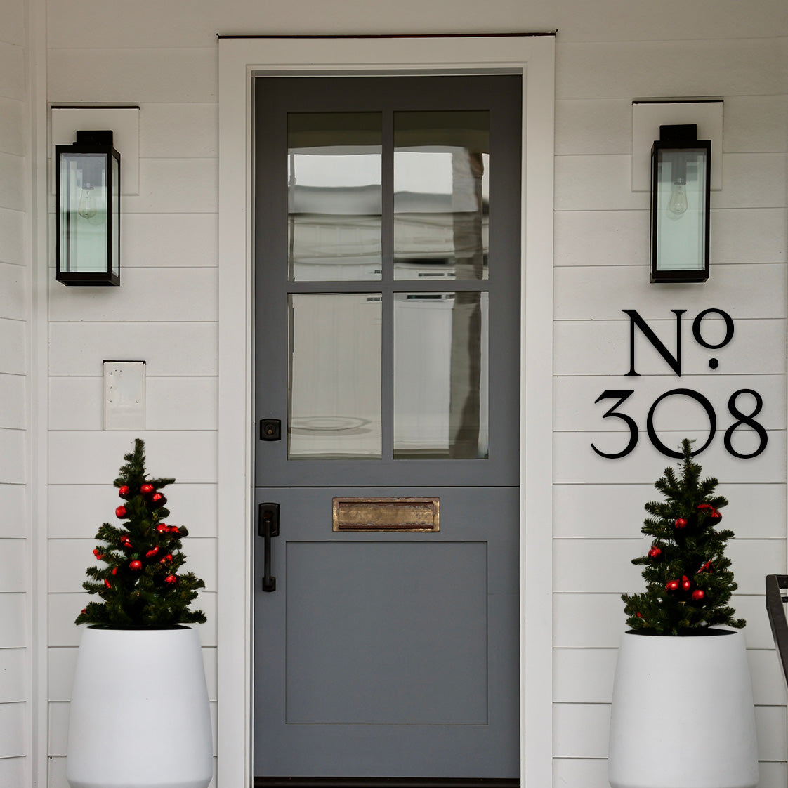 Gray front door with decorative Christmas trees and house number '308' black house numbers on a white wall.