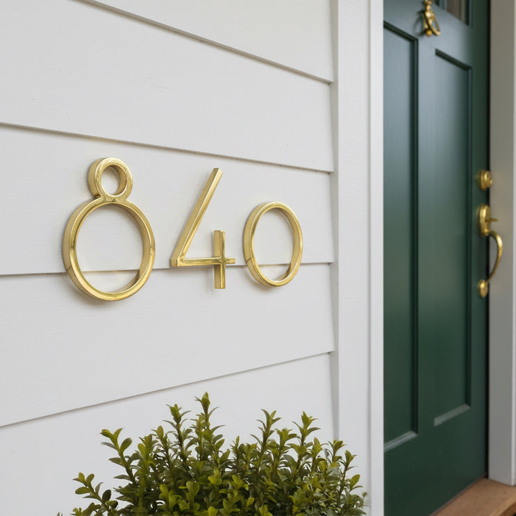 Gold house numbers '840' on a white wall with a green door.