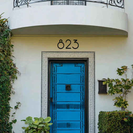 Blue door with decorative number '823' in black metal on a white building facade.