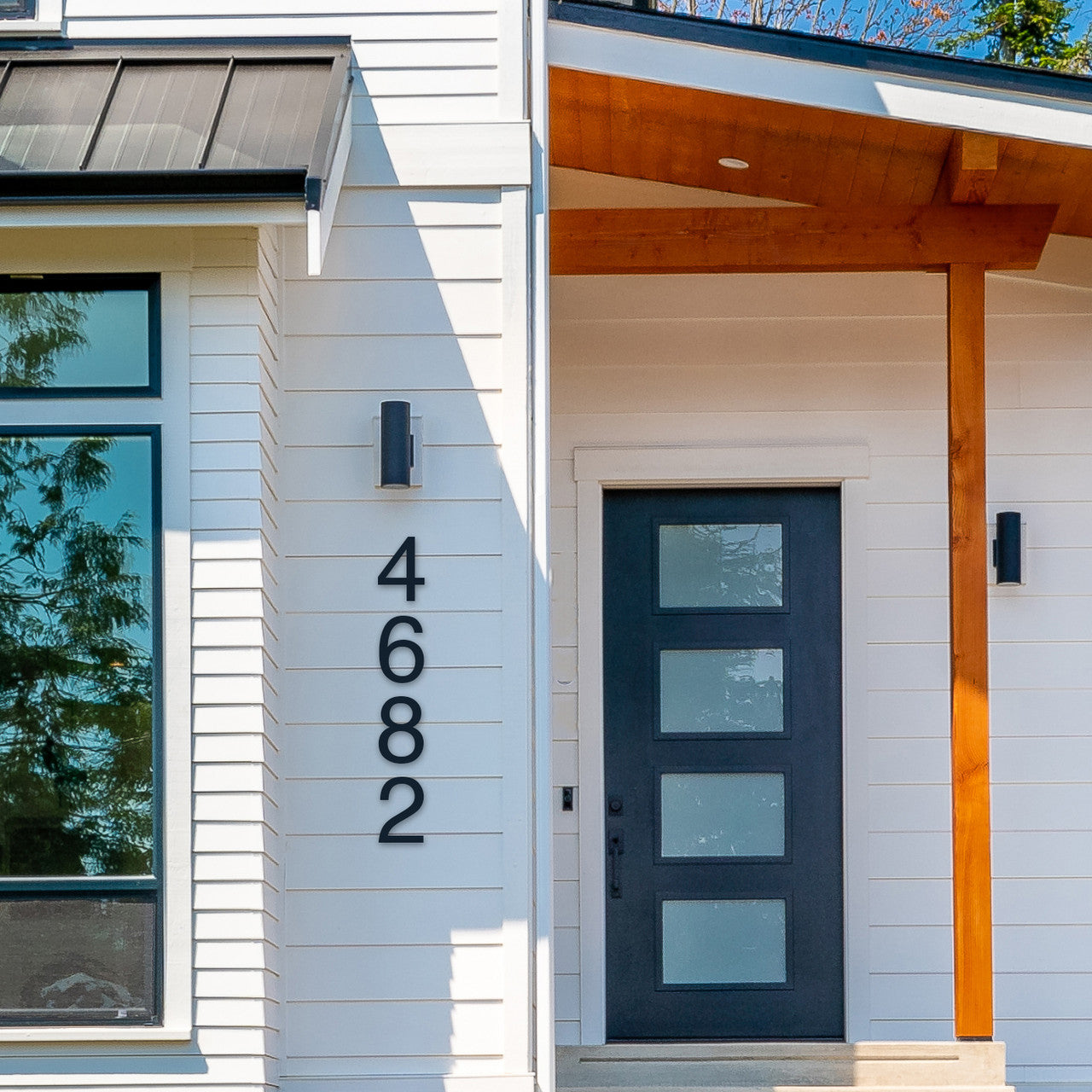 Modern black house numbers '4682' mounted on a white exterior wall, next to a dark door with a glass panel design.