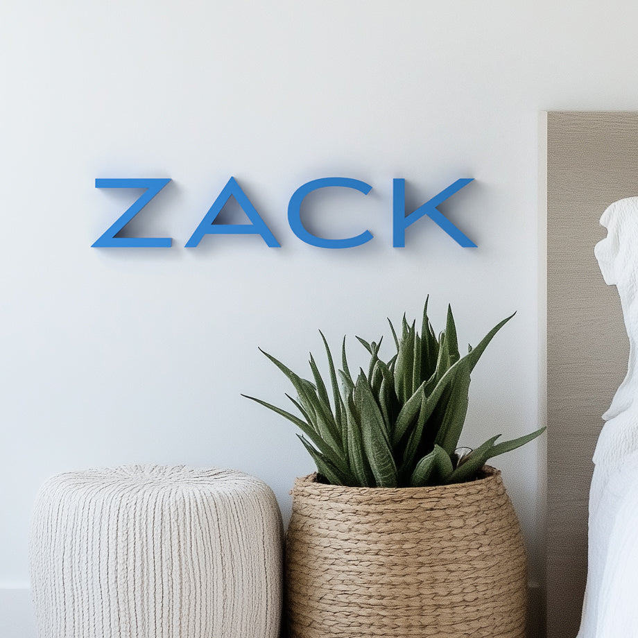 Custom personalized midcentury modern wall art with the name 'ZACK' in blue letters, displayed on a white wall above a potted plant and a woven basket.