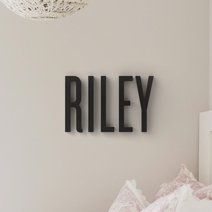 The image displays the word 'RILEY' personalized wall decor in bold, black letters mounted on a light-colored wall, likely within a child's room setting.