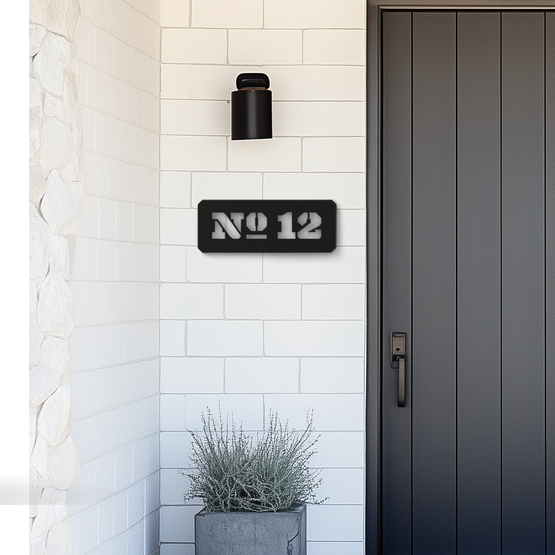A modern, black house number sign with the number 12 mounted on a white tiled wall above a black door.