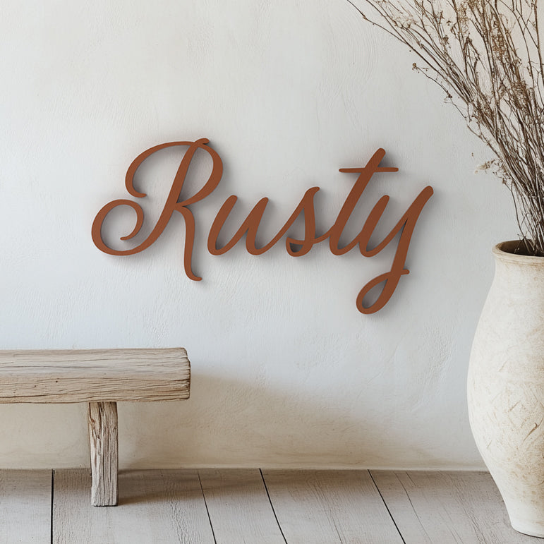 A customized acrylic wall art with the name Rusty written in a flowing cursive script, placed on a wall above a bench and a vase with dried plants.