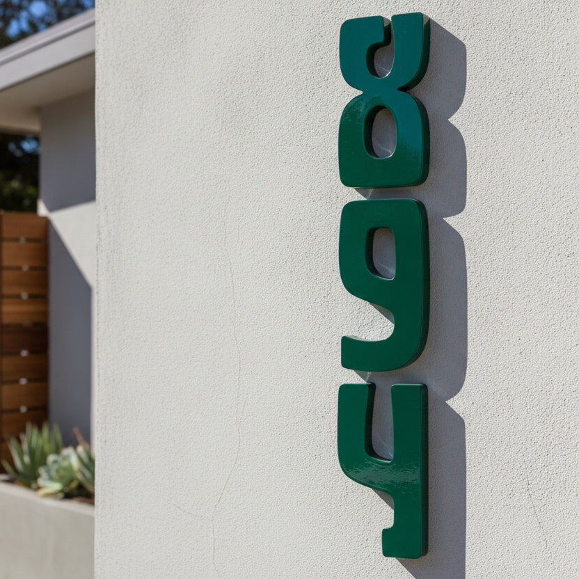 Dark green 3D metal house numbers reading '894' mounted vertically on a textured white stucco wall.
