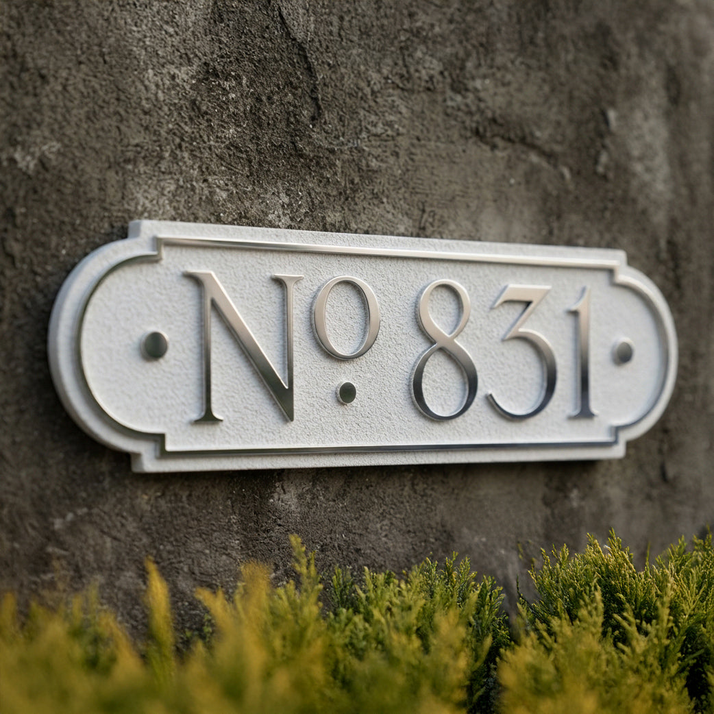 Decorative house number plaque displaying No.831 with raised lettering on textured concrete wall. Shown in: White · Cast Aluminum