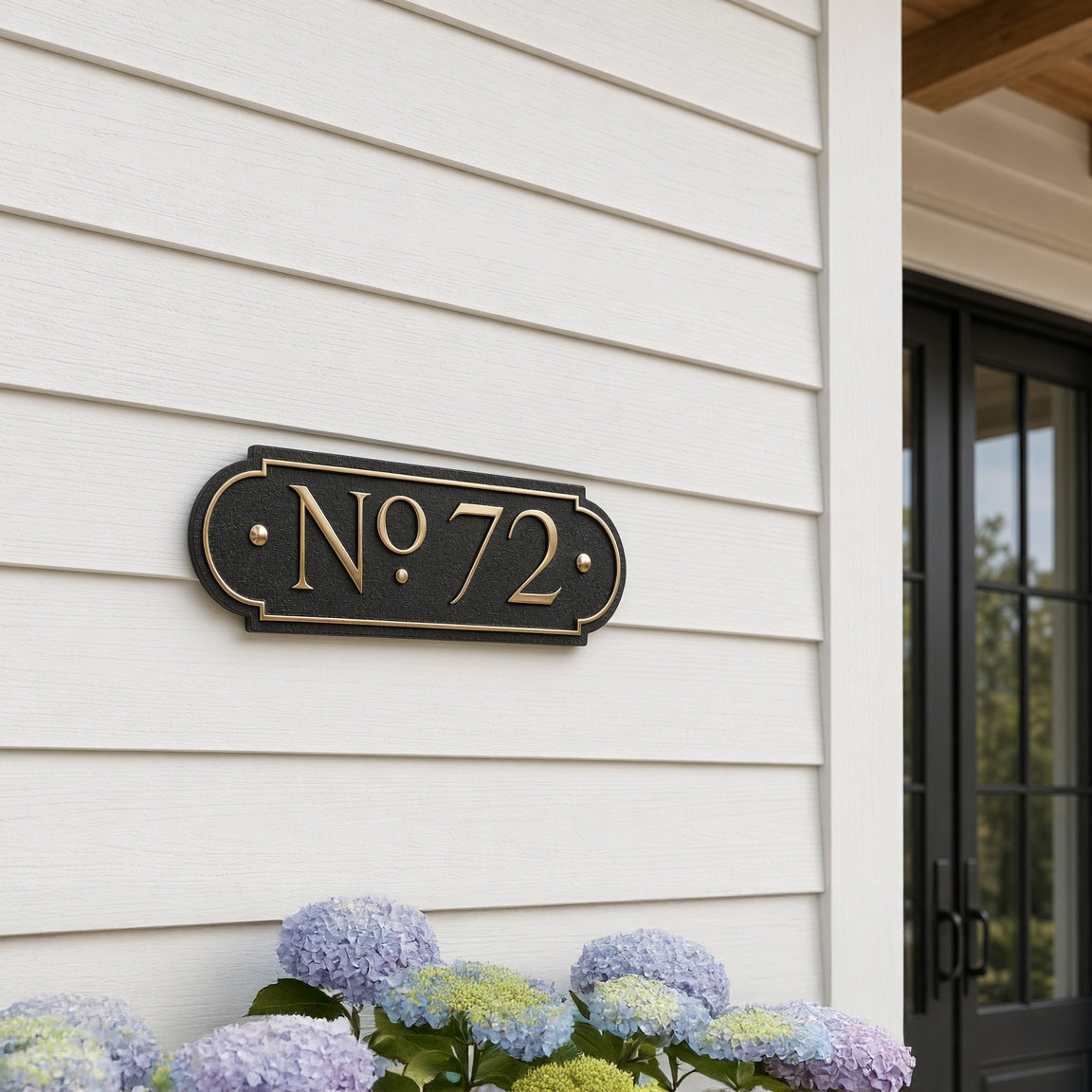 Traditional plaque displaying No. 72 in gold text on black background, mounted on white siding beside a door. Shown in: Black · Brass