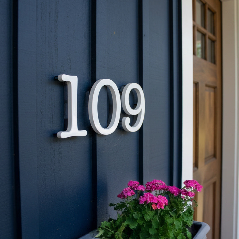 House number '109' on a blue door with pink flowers in the foreground