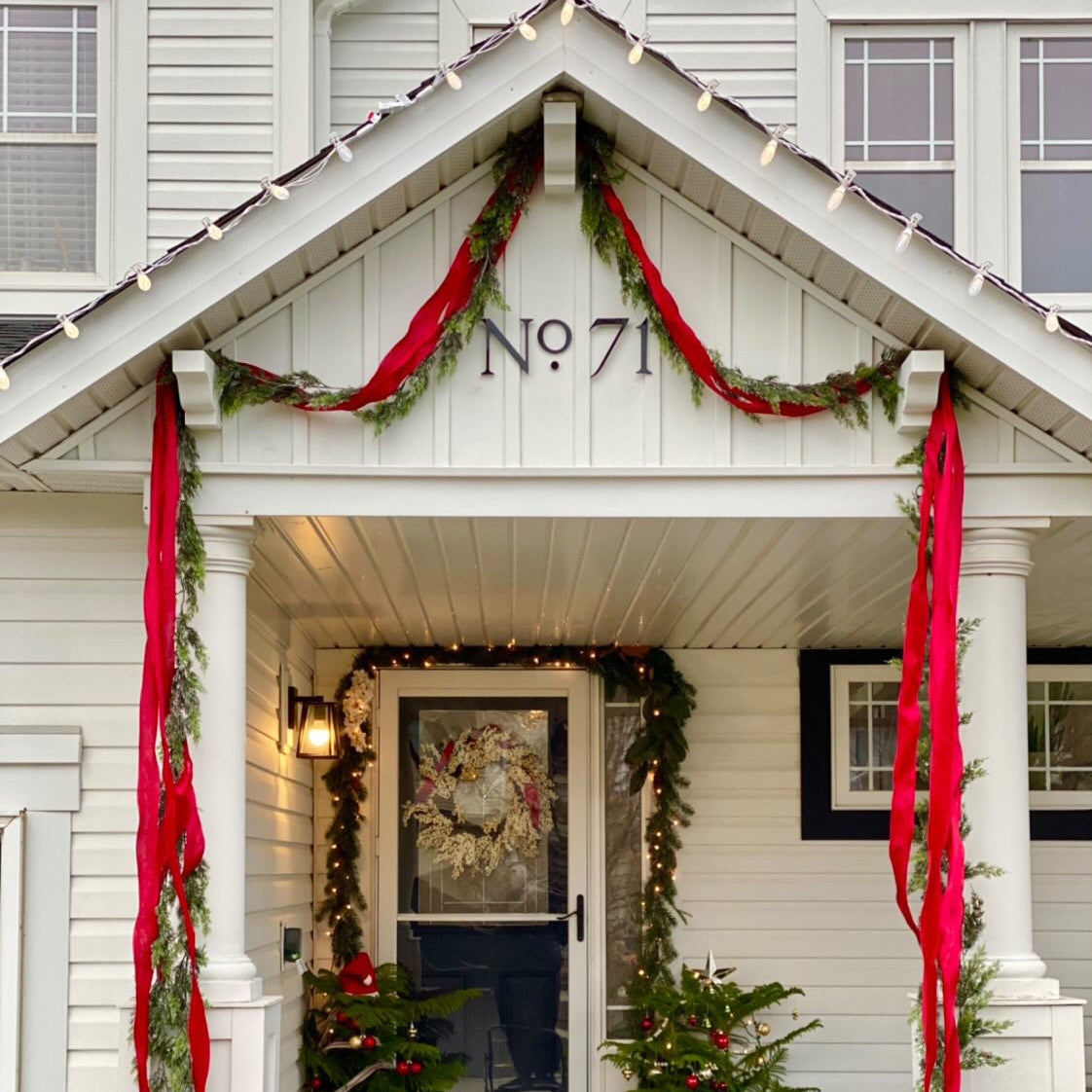 Decorative front porch of a house with Christmas decorations, including red ribbons and potted trees.