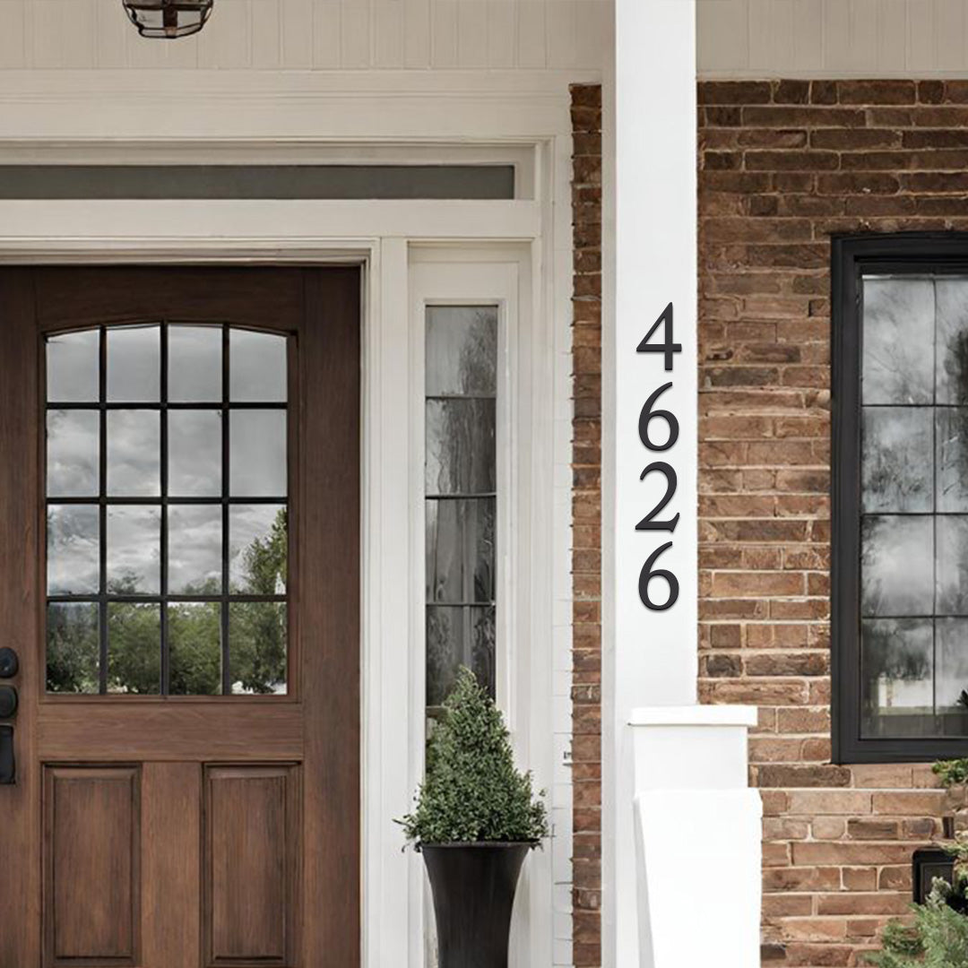 Black house numbers '4626' mounted on a white column beside a brown wooden door with glass panes, on a brick exterior background.