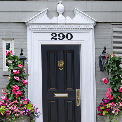 black house numbers above a black and brass door and painted grey brick house