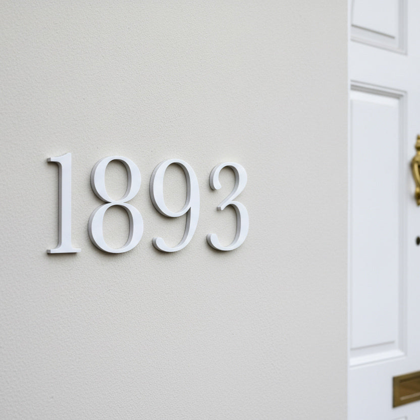 White 3D house number '1893' mounted on a textured off-white exterior wall next to a white front door.