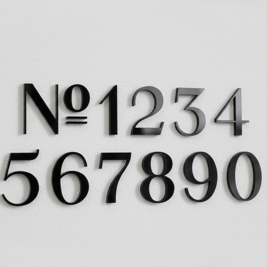 Black modern house numbers N°1234567890 displayed on white wall showing Flora font style. Shown in: Gloss Black · 1/4" Acrylic