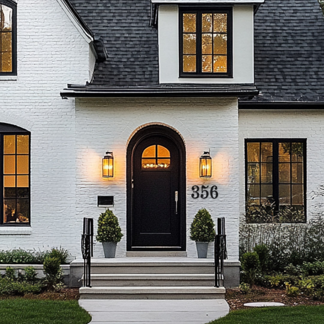 Black metal house numbers in a traditional style on a  white brick house with an arched black front door
