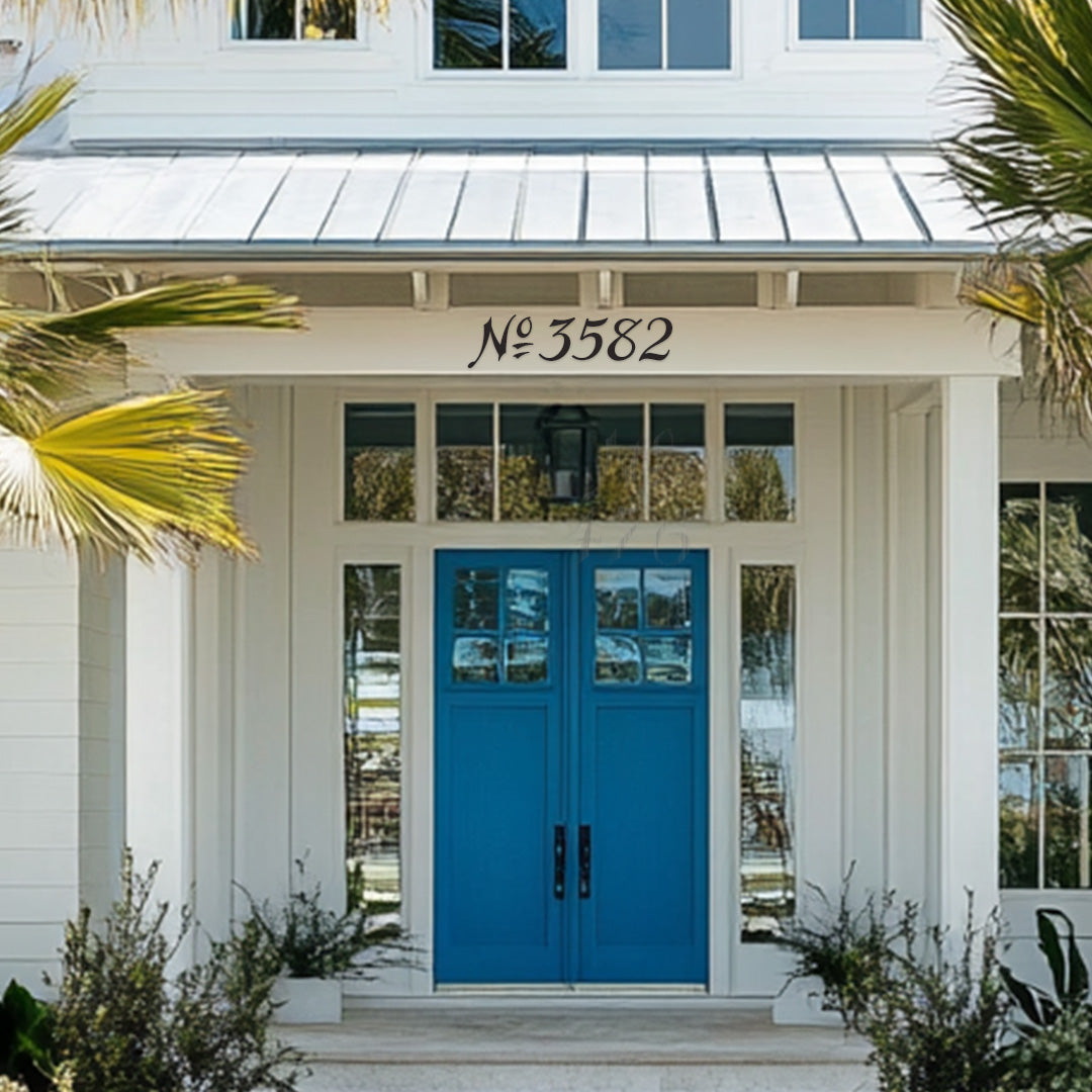 A white beach house with a blue door, featuring custom house numbers '3582' in a sans serif font, mounted above the door.