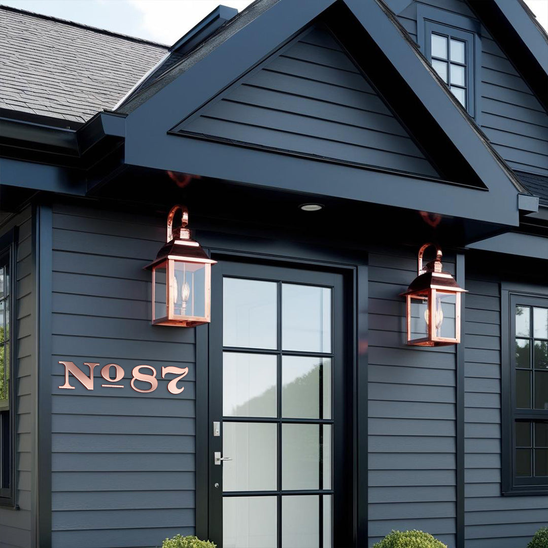 Black house with solid copper house numbers 'No 87' mounted on the exterior wall near the entrance, featuring a traditional design. Copper lanterns