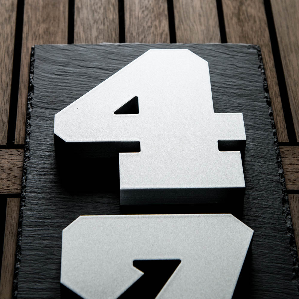 A close-up of metallic silver house numbers '4' placed on a black background, with a wooden surface in the backdrop.