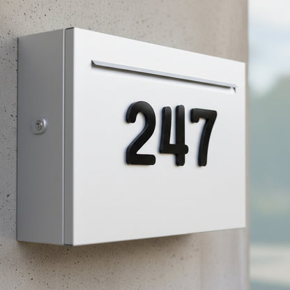 White mailbox with black numbers '247' mounted on a concrete wall.