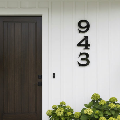Dark wooden door with house numbers '943' on a white wall, featuring green flowers.