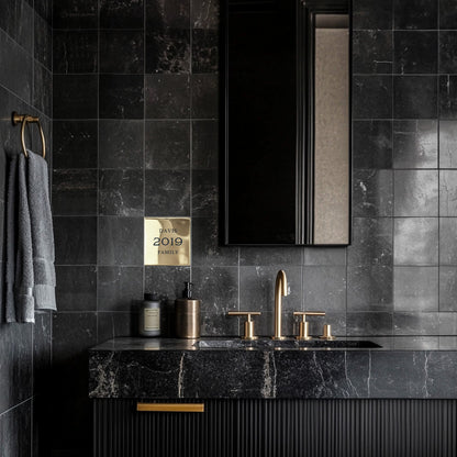 A black tiled bathroom wall featuring a custom brass accent plaque grouted into the tile with the text 'Davis 2019 family' displayed in a traditional style font.