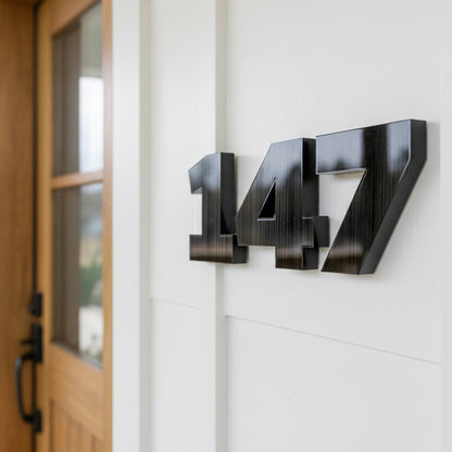 Black house numbers '147' on a white wall next to a wooden door.