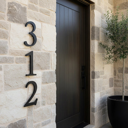 Modern house number '312' on a stone wall with a dark door and potted plant.