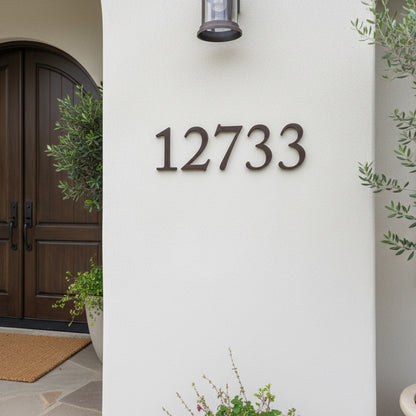House number '12733' on a white wall with a wooden door and plants.