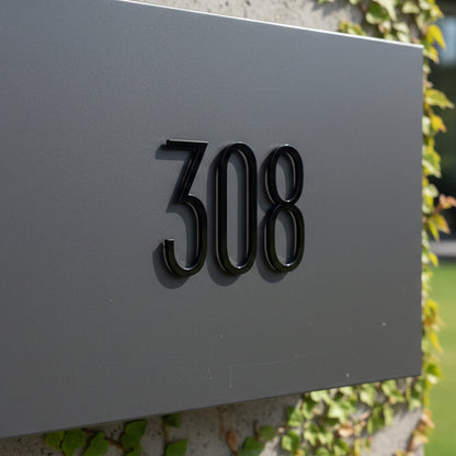 House number '308' on a gray mailbox with greenery in the background