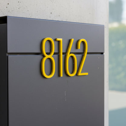 Gray mailbox with yellow house numbers '8162' on a blurred outdoor background