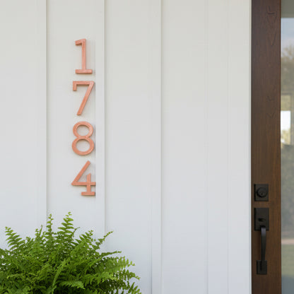 pink House numbers '1784' on a white door with a plant in the foreground