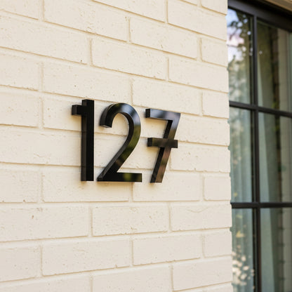 Modern house numbers '127' on a light brick wall.