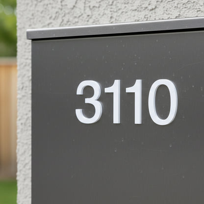 Modern house number '3110' on a gray plaque against a textured wall.